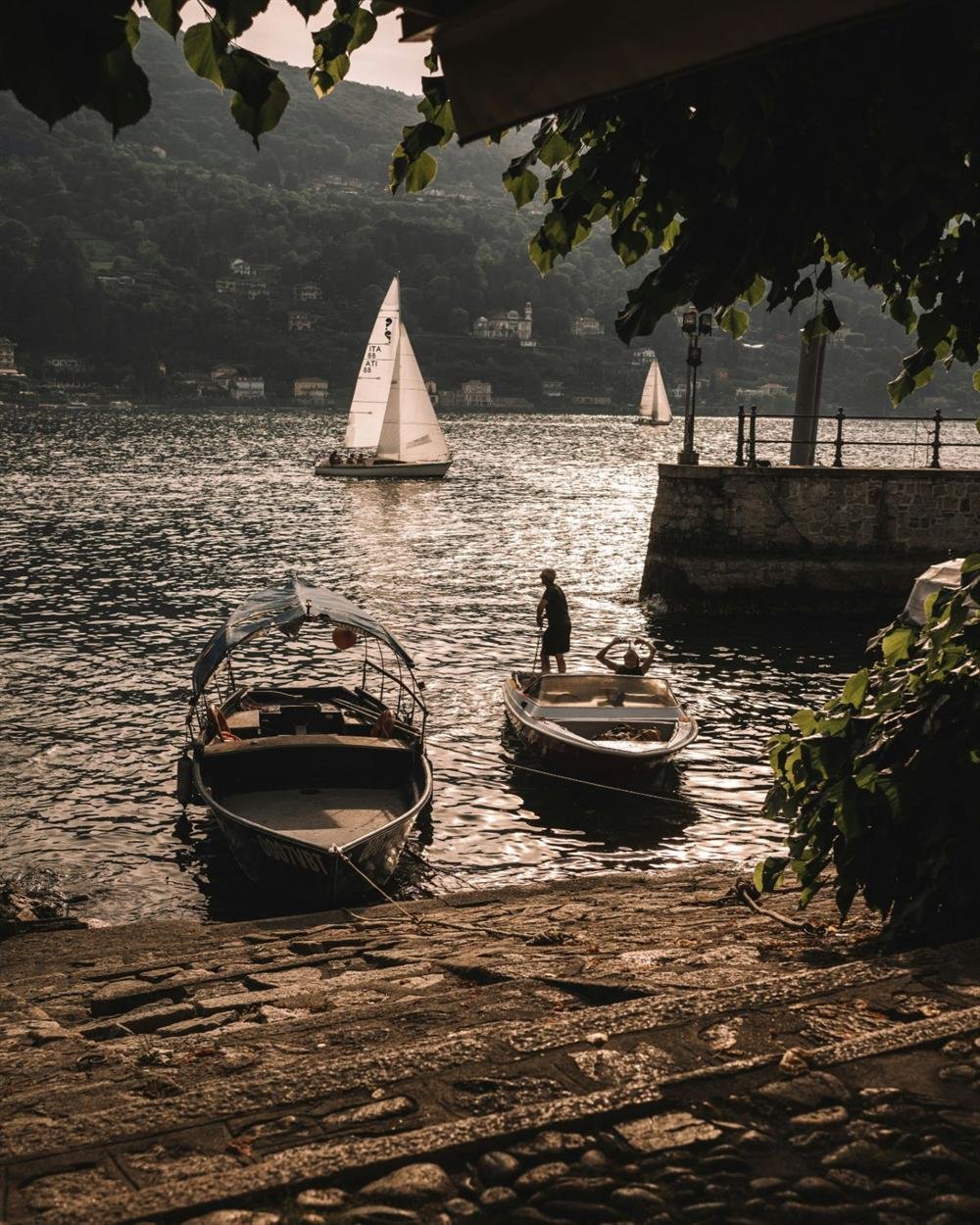 Veleiros em um lago ao entardecer, vistos de um cais de pedra